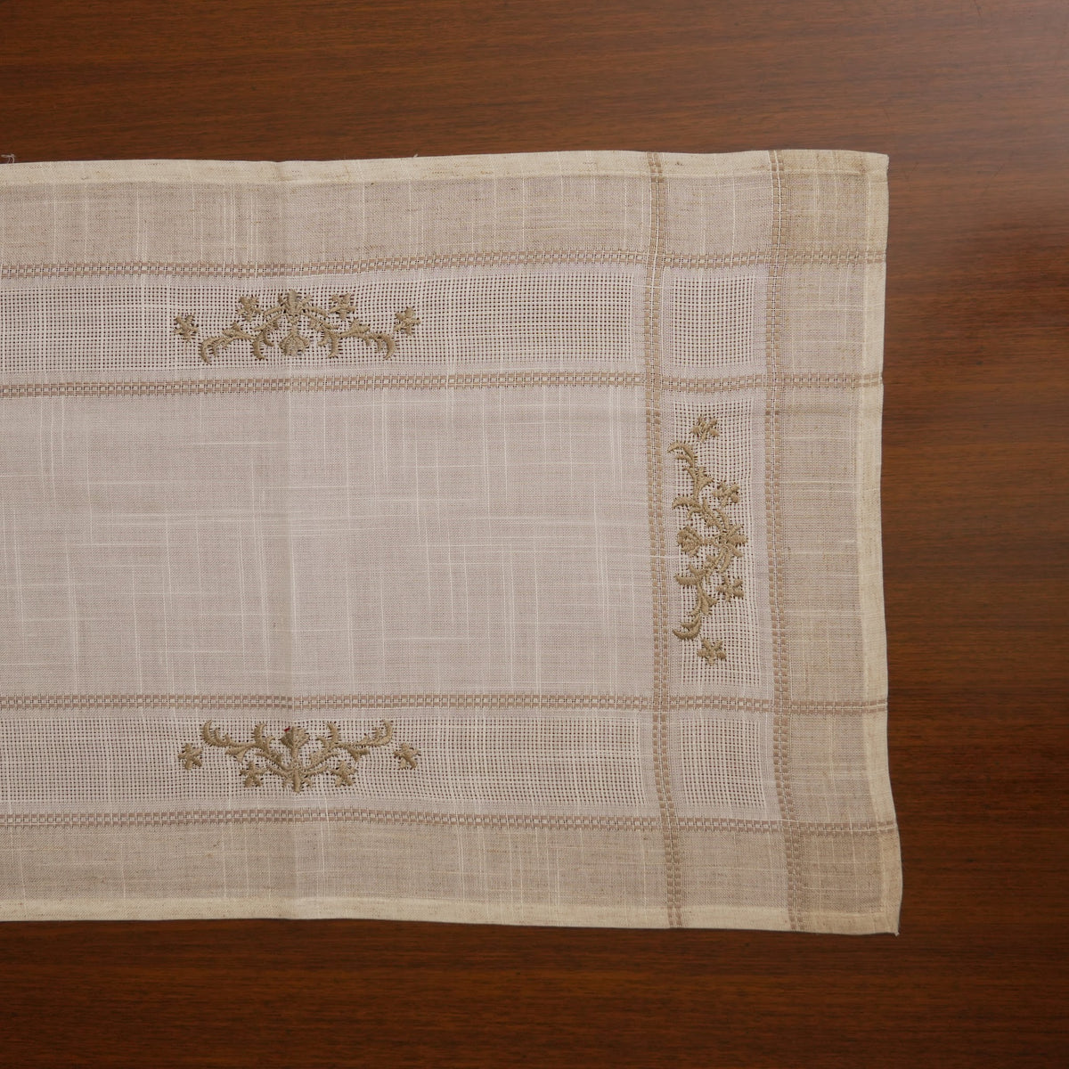 Linen table runner laid flat showing olive cross-stitch sprigs